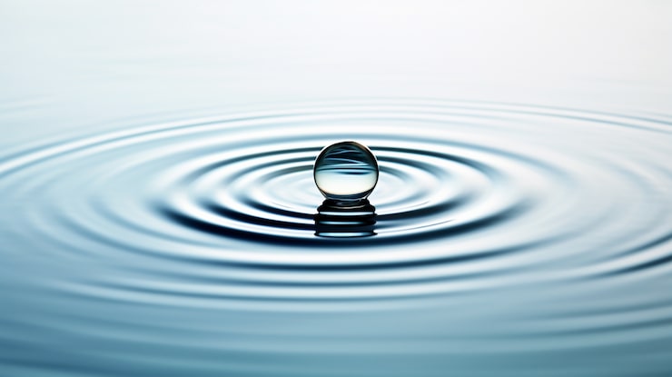 Nahaufnahme eines einzelnen Wassertropfens, der eine perfekte Welle auf einer ruhigen Oberfläche erzeugt